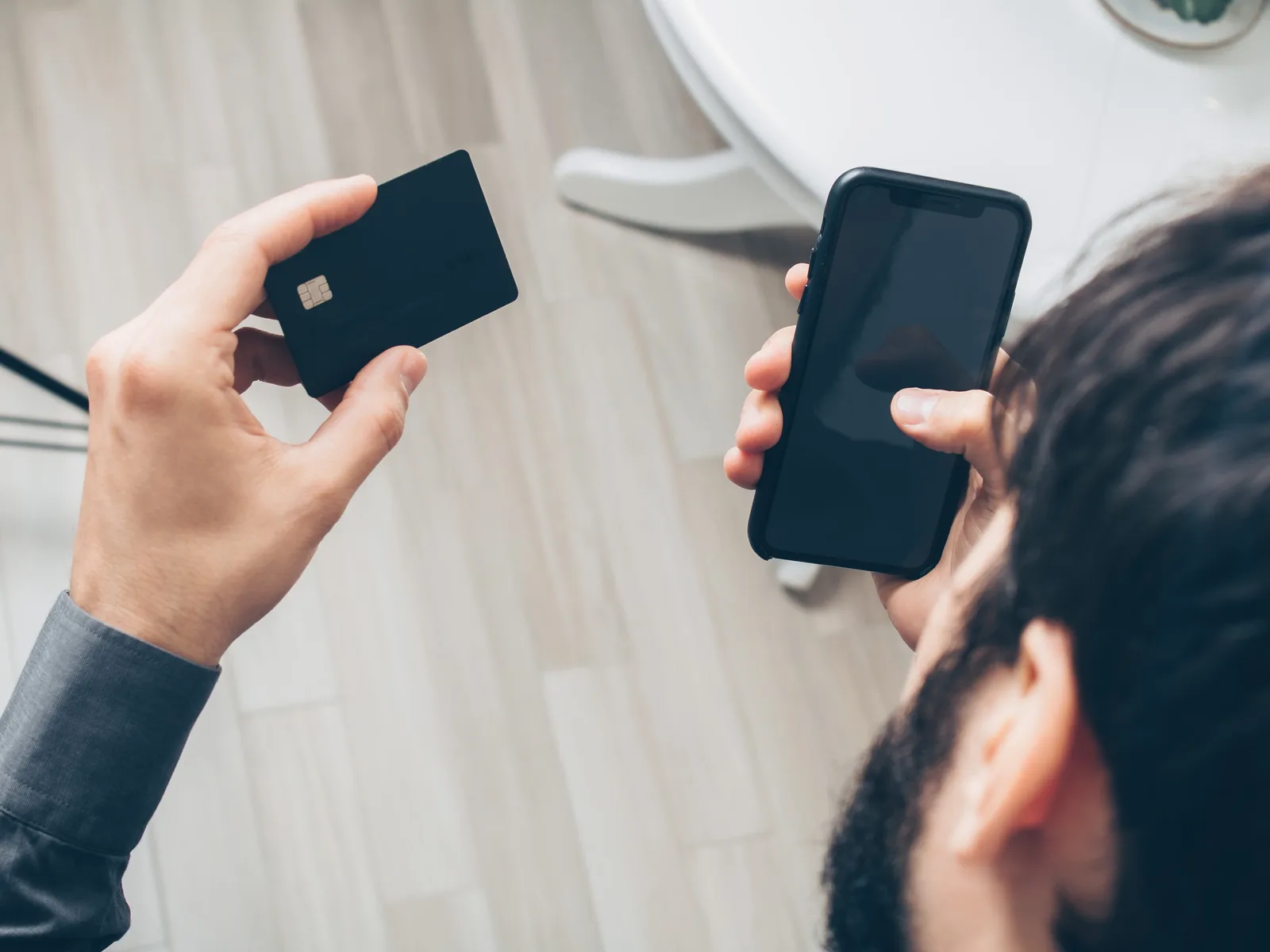 Close-up of man holding a smartphone and credit card, making an online payment indoors.