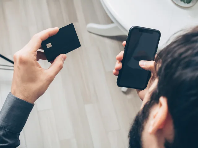 Close-up of man holding a smartphone and credit card, making an online payment indoors. Sikkerhedskrav til betalinger i danske webshops